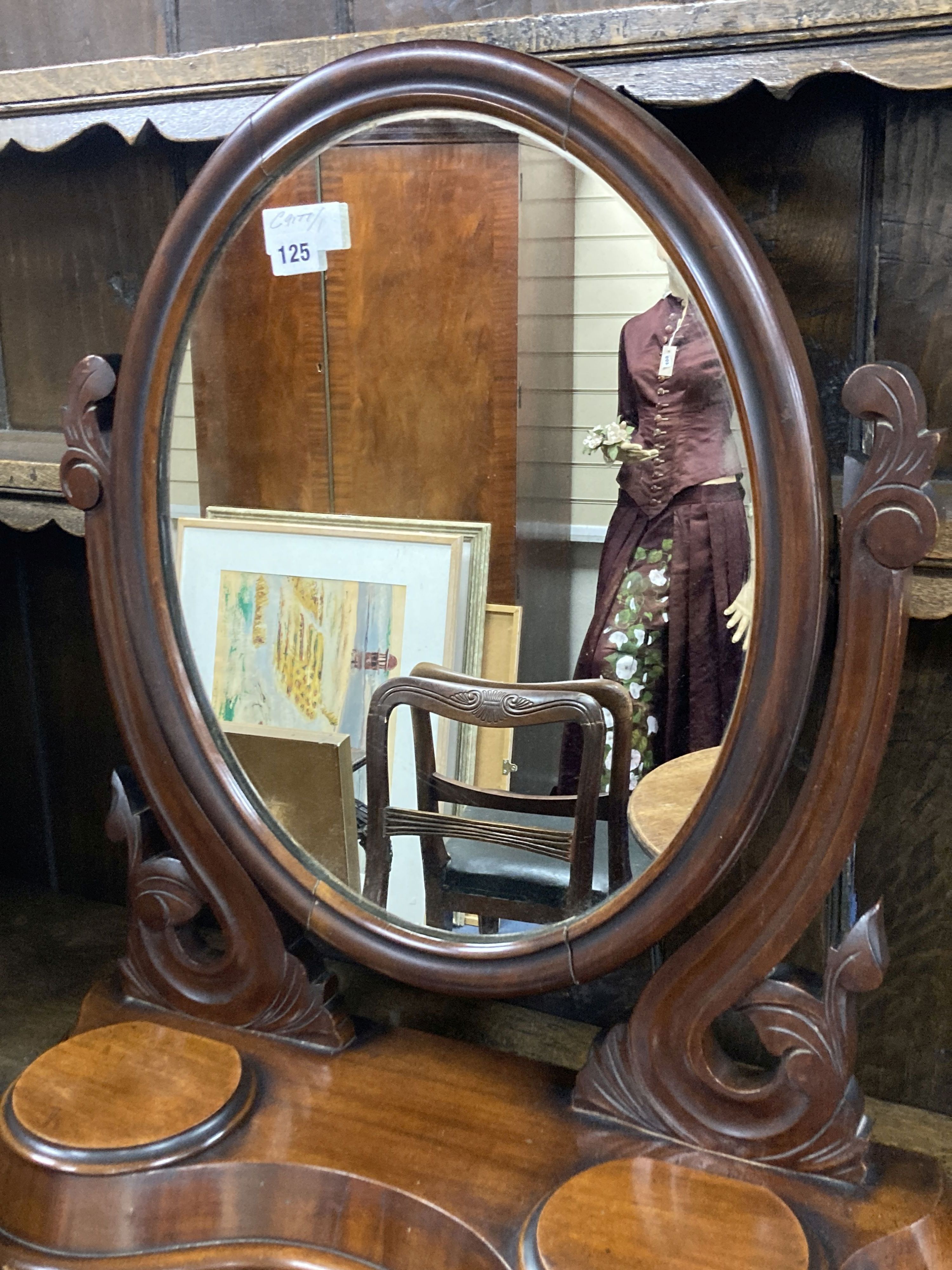 A Victorian mahogany toilet mirror of oval form above a raised platform with twin lidded compartments, width 63cm, height 71cm